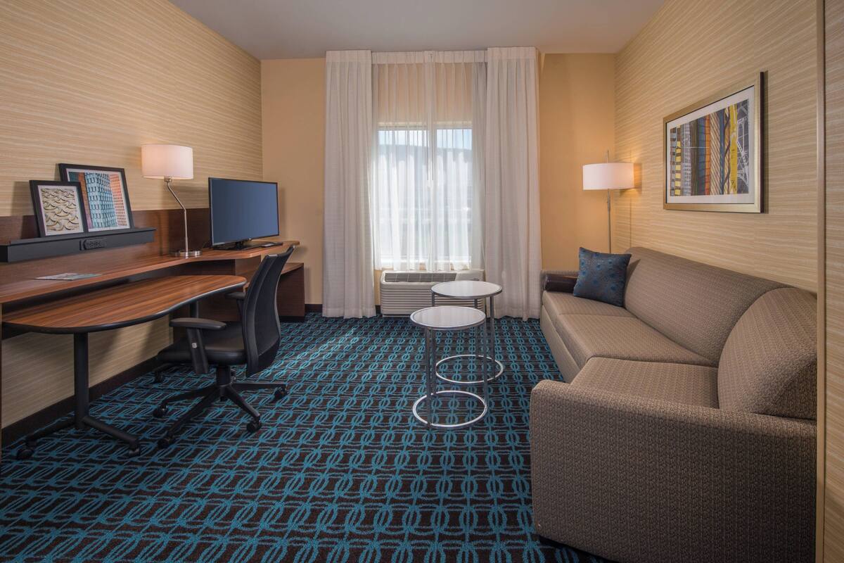 Une chambre d’hôtel avec un bureau en bois, une télévision, un canapé et une moquette à motifs.