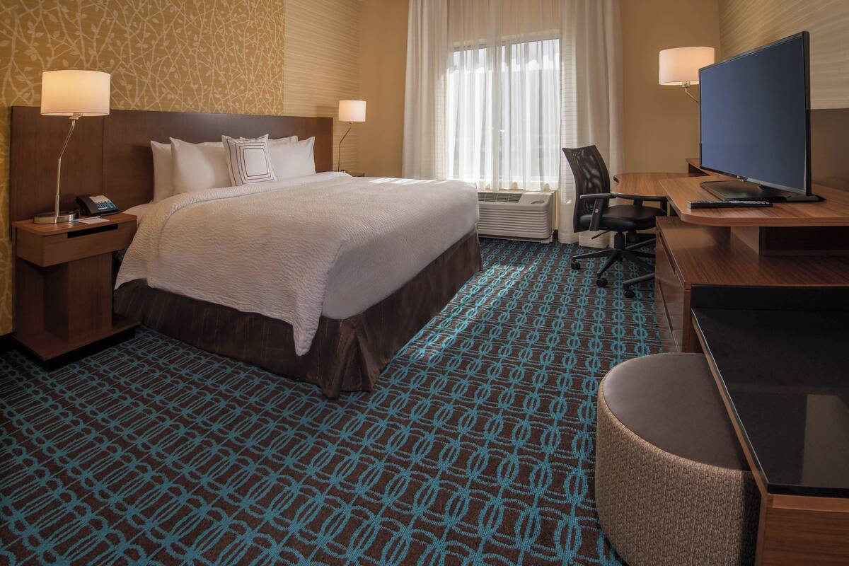 Une chambre d’hôtel avec un grand lit, un bureau avec une télévision, une chaise et une lampe de bureau.