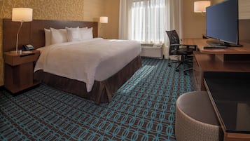 Una habitación de hotel con una cama grande, un escritorio con televisor, una silla y una lámpara de escritorio.