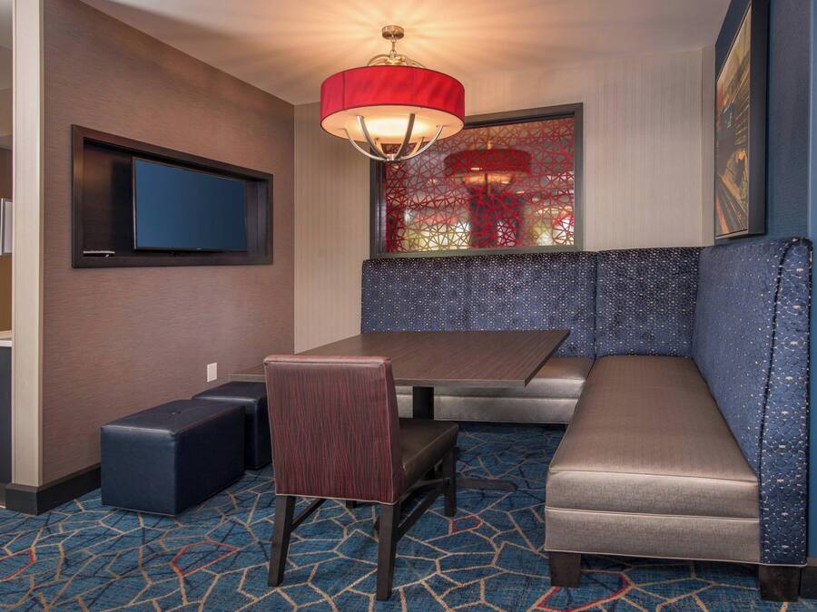 A hotel room with a large bed, a seating area with a bench and a chair, a television mounted on the wall, and a patterned carpet.