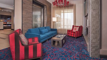 A modern hotel lobby with a blue sofa, a red armchair, a patterned carpet, and a chandelier.