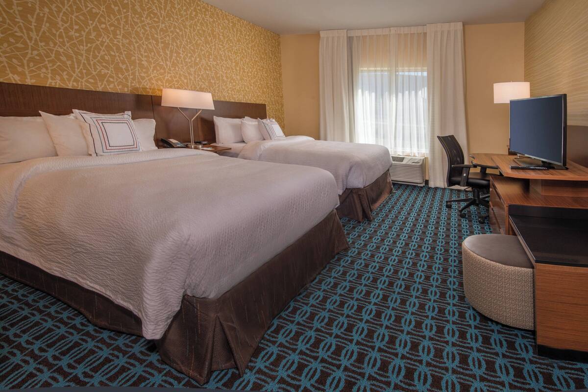 Une chambre d’hôtel avec deux lits, un bureau avec un ordinateur et une chaise.