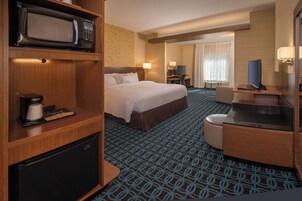 A hotel room with a bed, a desk, a television, a microwave, and a refrigerator.