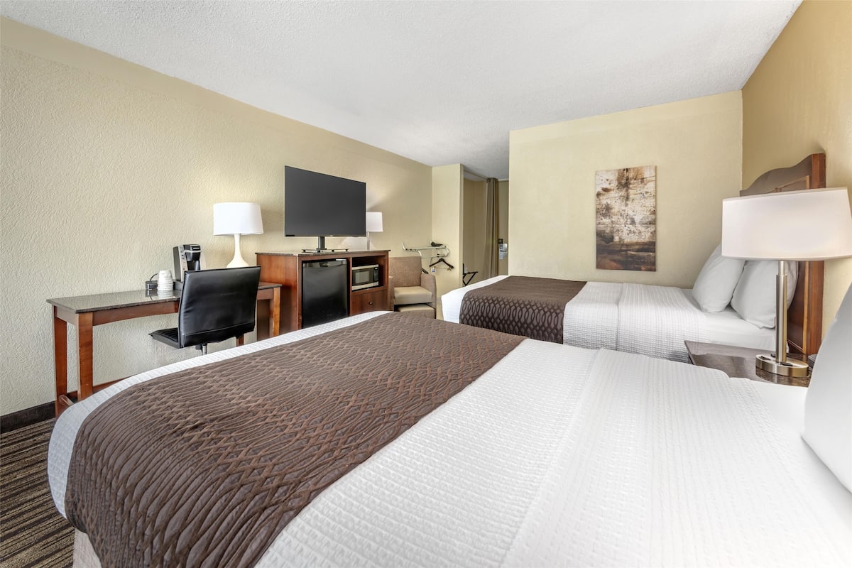 A hotel room with two beds, a desk, a TV, and a chair.