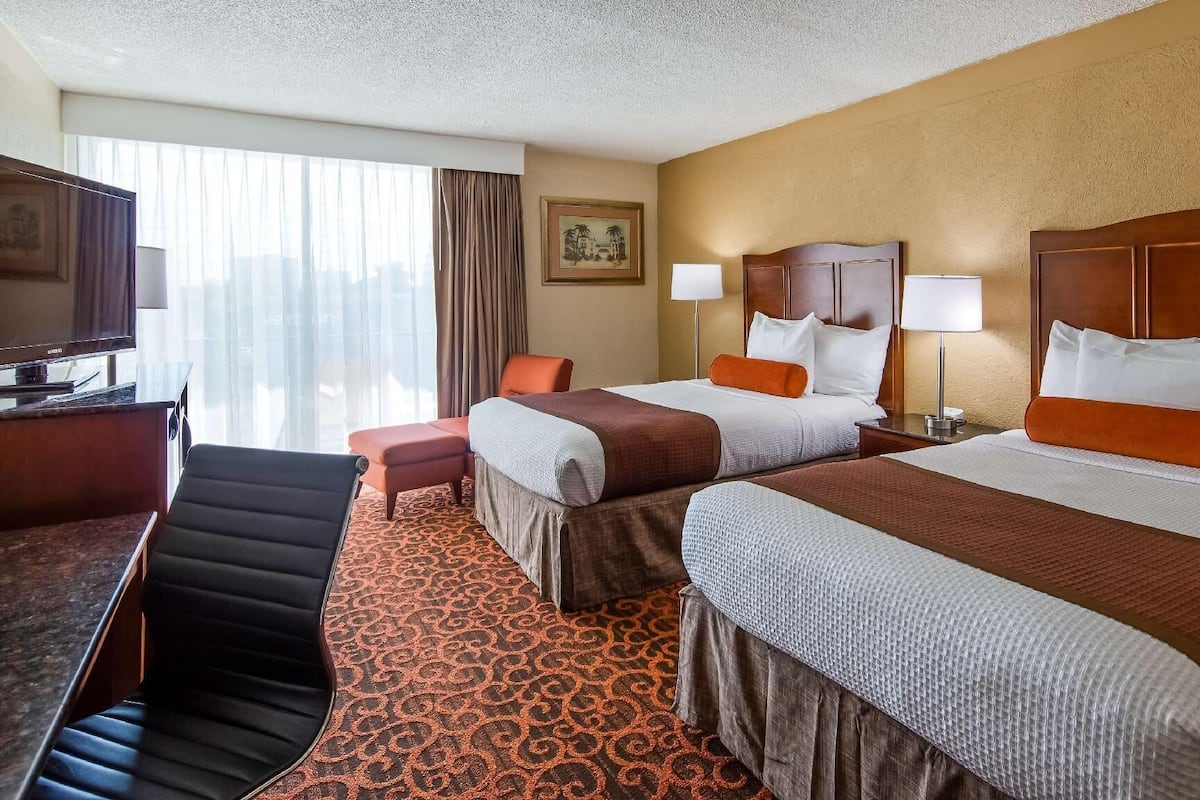 A hotel room with two beds, a desk, a chair, and a television.