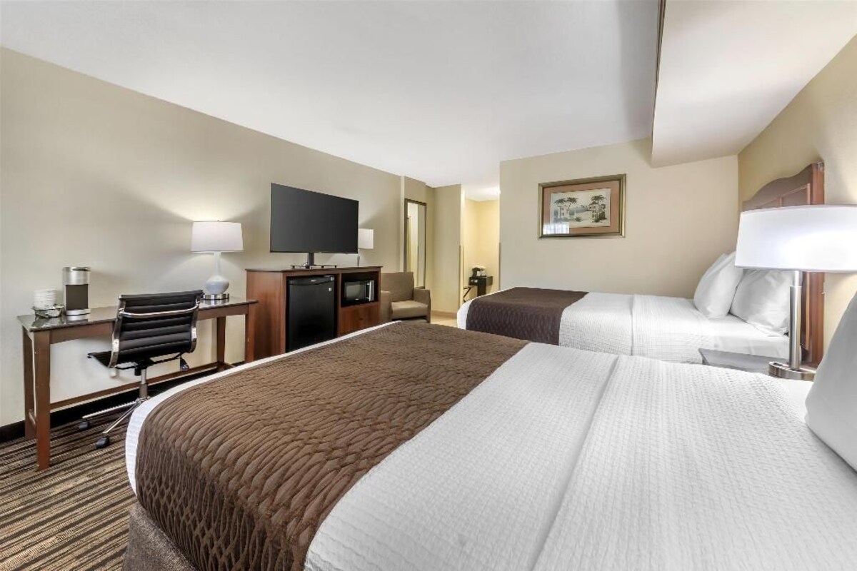 A hotel room with two beds, a desk, a television, and a framed picture on the wall.