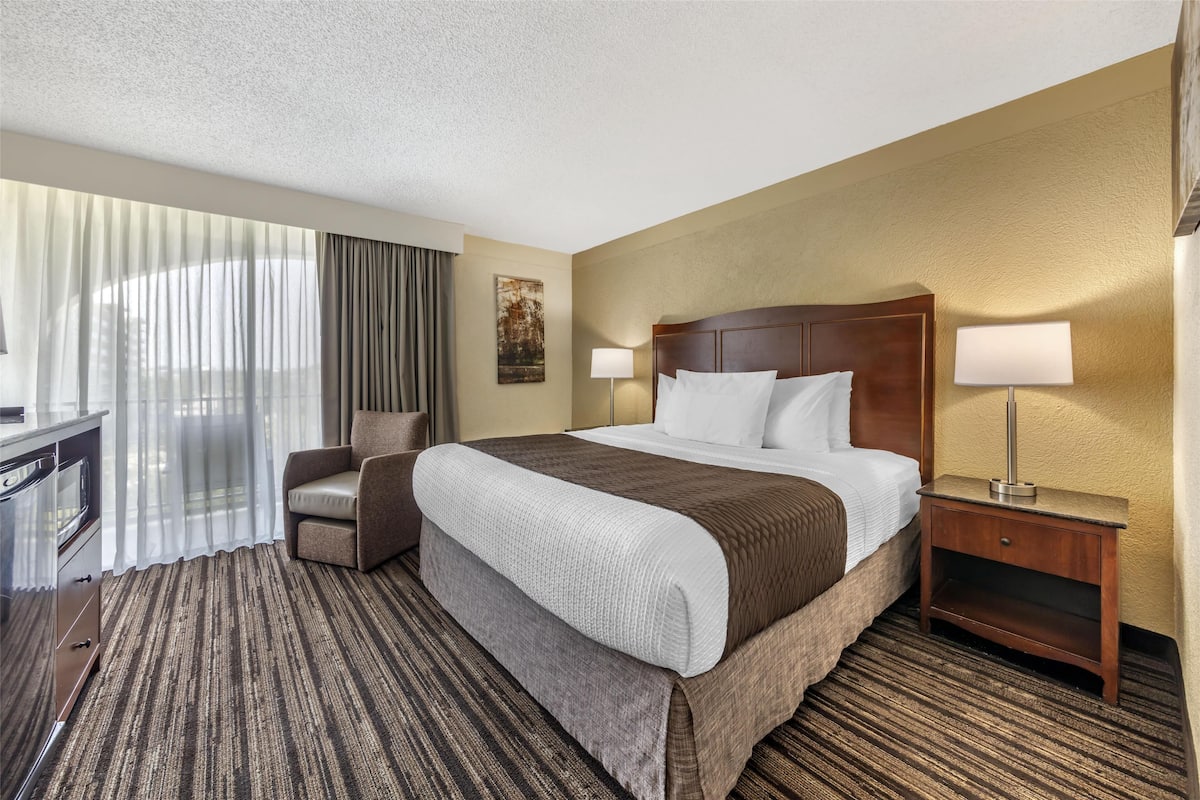 A hotel room with a large bed, a desk, a chair, and a nightstand with lamps.