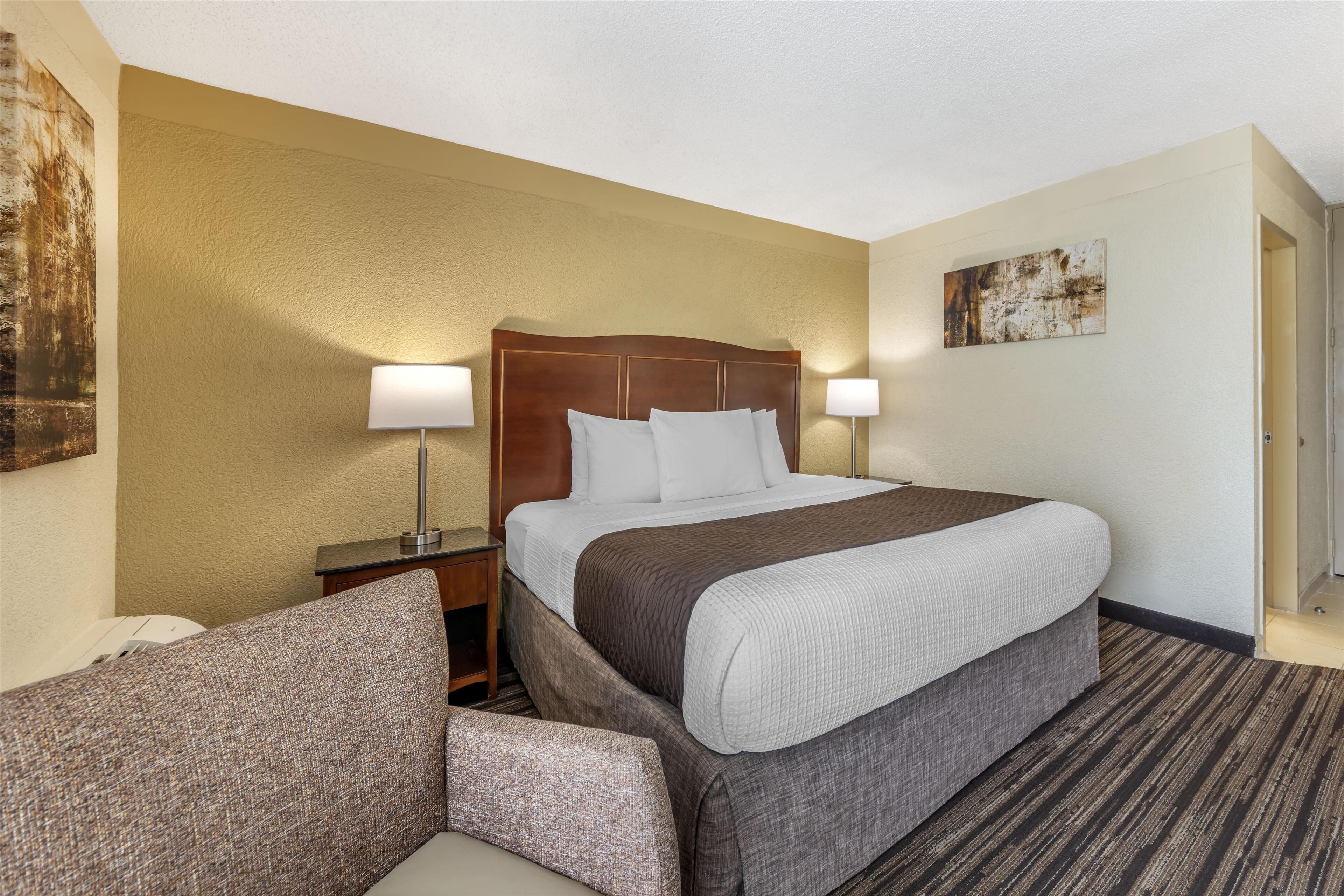 A hotel room with a large bed, two bedside lamps, a nightstand, a couch, and a painting on the wall.