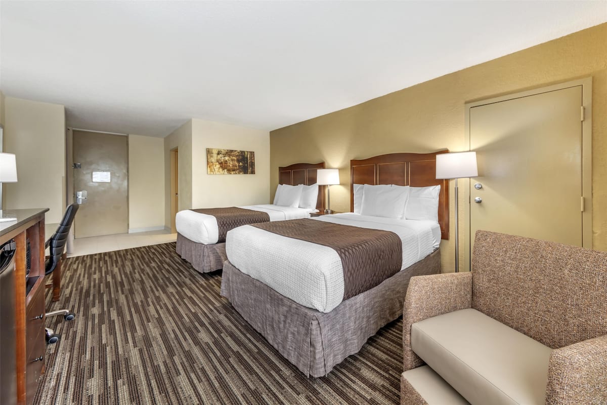 A hotel room with two beds, a desk, a chair, and a door.
