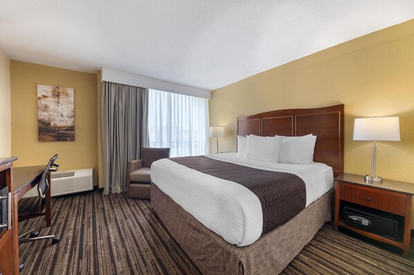 A hotel room with a large bed, a desk with a chair, a lamp, and a painting on the wall.