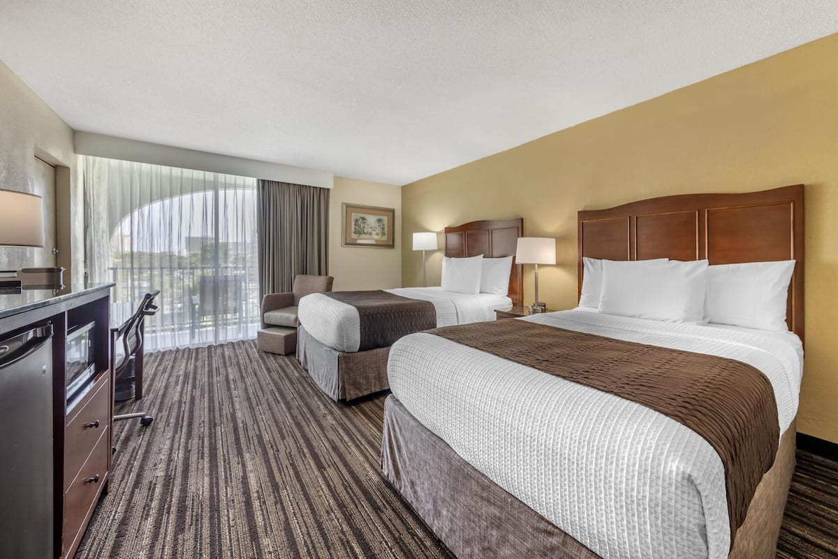 A hotel room with two beds, a desk, a chair, and a large window with curtains.