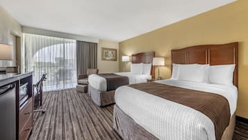 Habitación de hotel con dos camas, un escritorio, una silla y un ventanal con cortinas.