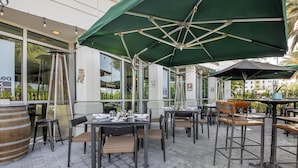 An outdoor dining area with tables and chairs, umbrellas, and a brick floor.