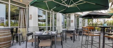 An outdoor dining area with tables and chairs, umbrellas, and a brick floor.