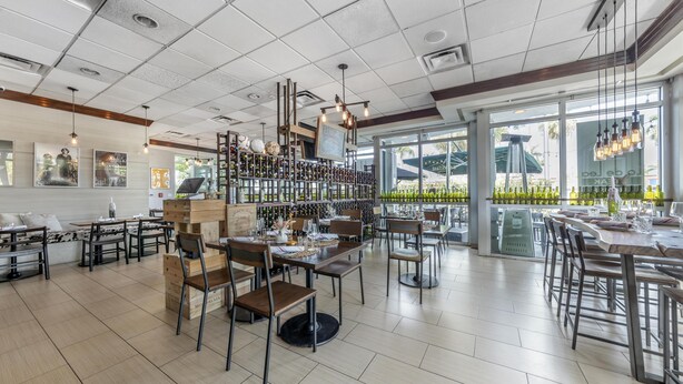 A modern restaurant interior with high ceilings, exposed ductwork, and a variety of seating arrangements including tables and chairs.