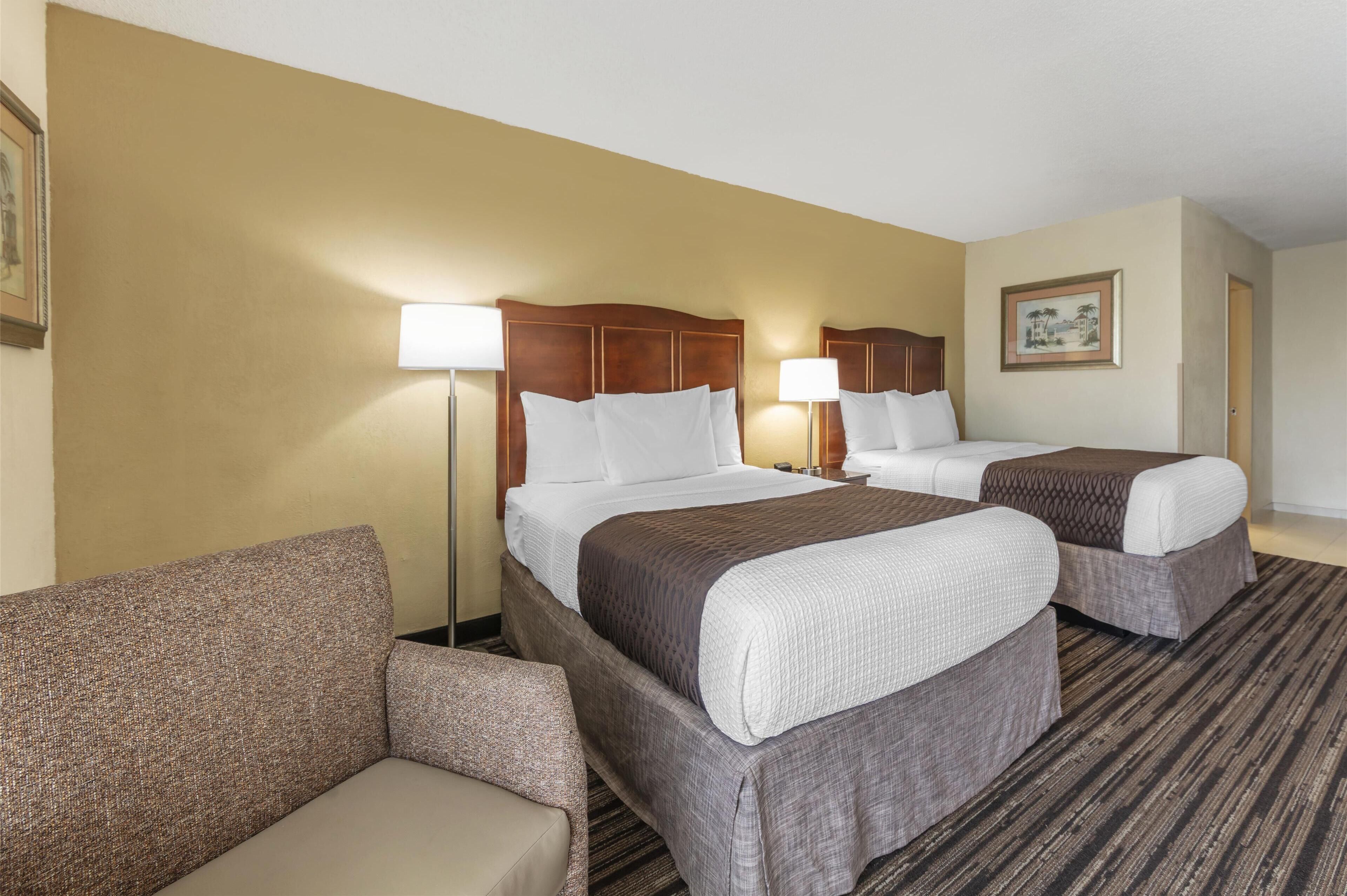 A hotel room with two beds, a sofa, and a nightstand with a lamp.