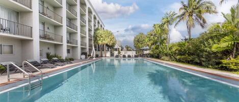 Une piscine avec des chaises longues et un bâtiment doté de nombreux balcons.