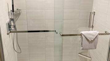 Une douche moderne dotée d’une porte en verre, d’un pommeau de douche à main et d’un porte-serviettes sur lequel est posée une serviette pliée.