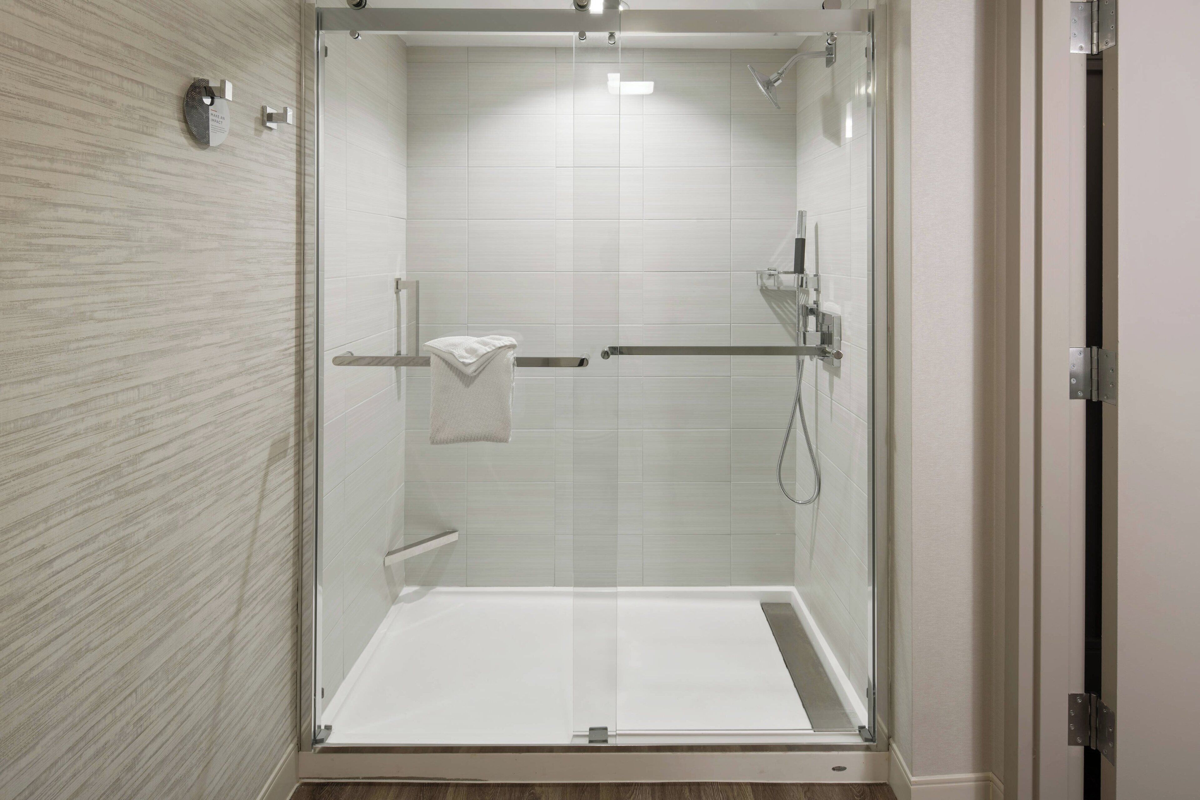 A modern shower enclosure with a glass door, a towel rack, and a handheld showerhead.