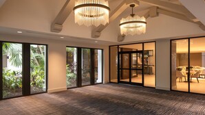 A spacious room with large windows, a carpeted floor, and two chandeliers.