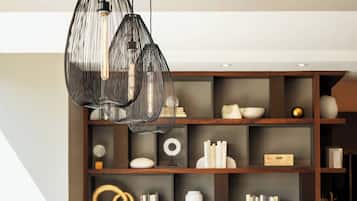 Un comedor moderno con una mesa de madera y sillas tapizadas en rojo, una estantería de madera oscura con diversos objetos decorativos e iluminación colgante.