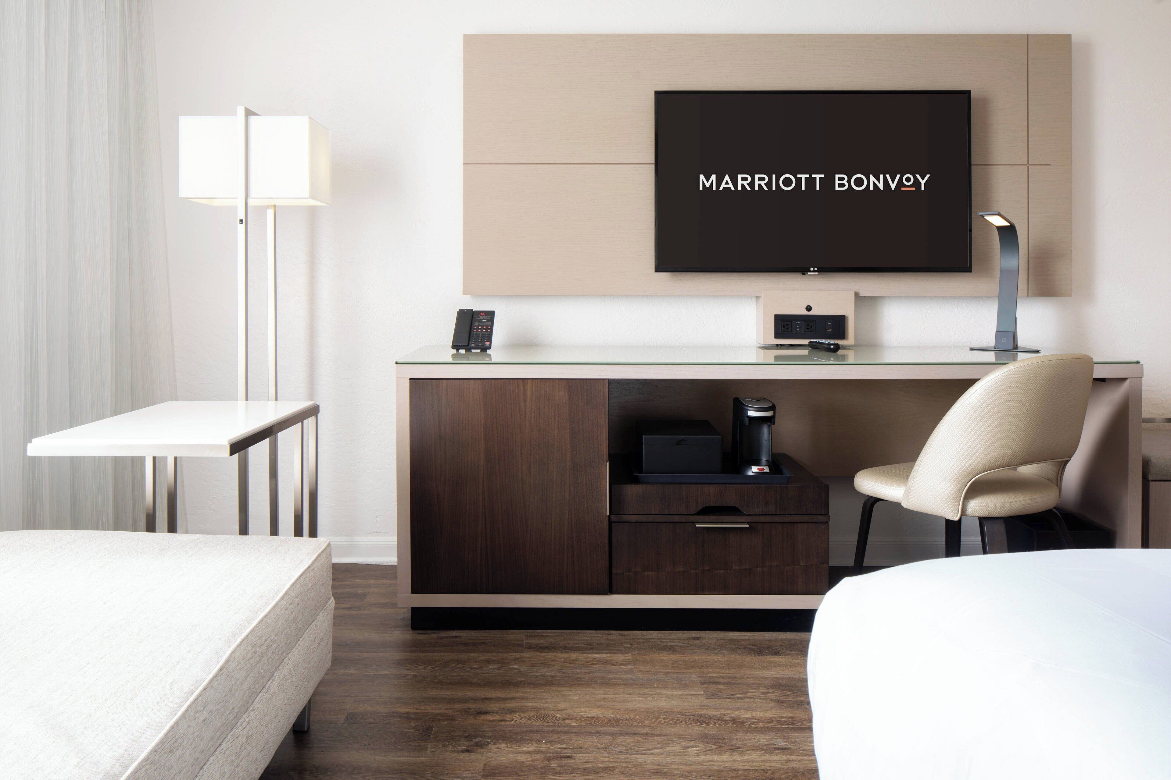 Habitación de hotel con cama, escritorio, televisor de pantalla plana, cafetera y una silla.