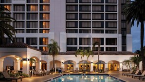 A hotel with a swimming pool, lounge chairs, and palm trees.