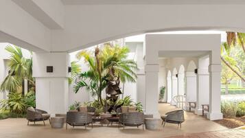 Un espacio al aire libre con mobiliario de mimbre, palmeras y una pieza decorativa central.