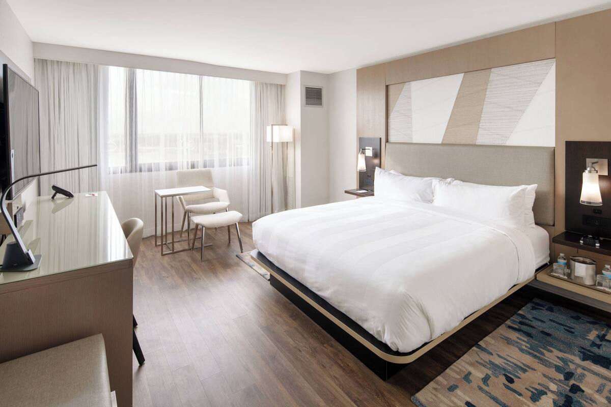 Een hotelkamer met een groot bed, een bureau met stoel, een televisie en een raam met gordijnen.