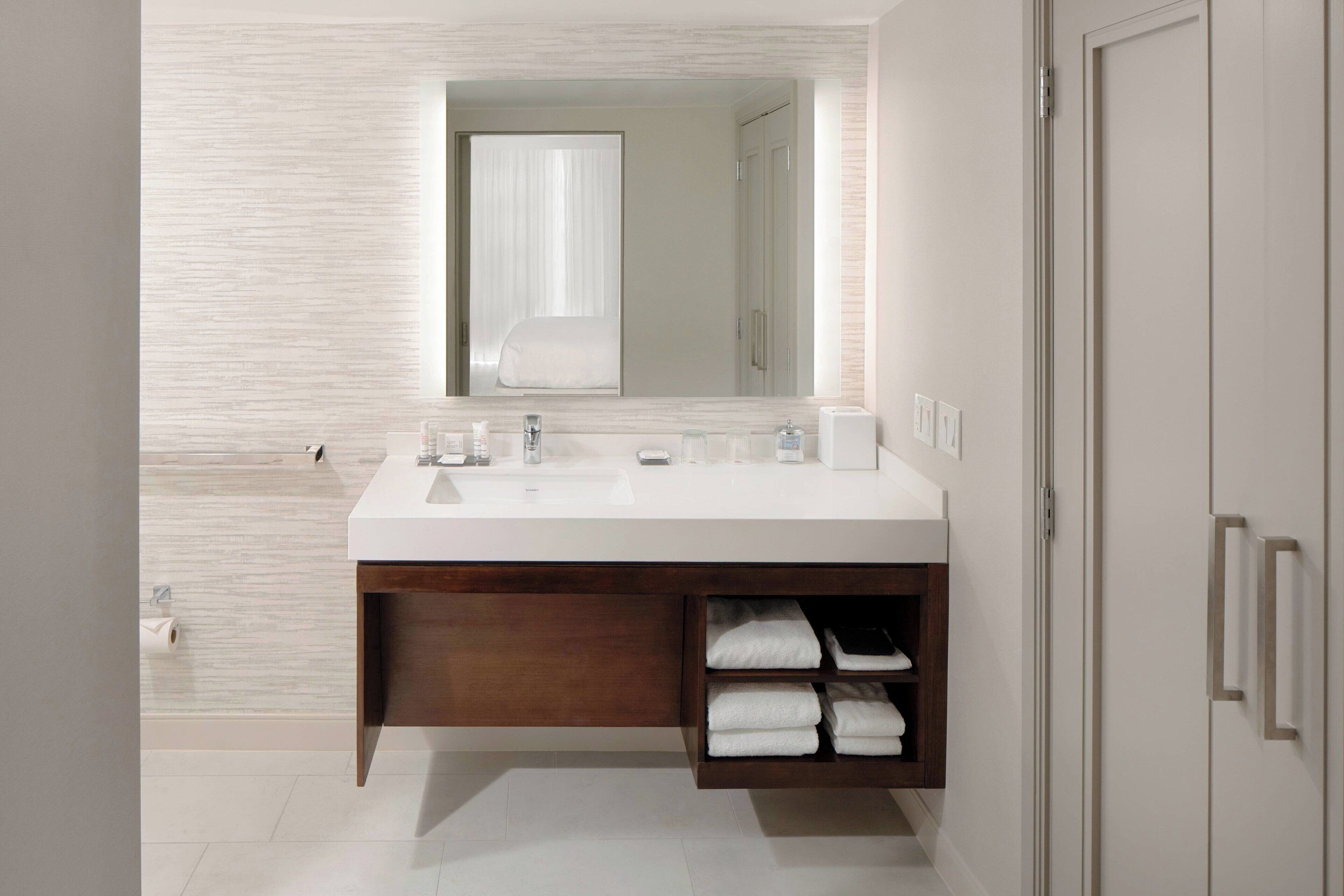 Une salle de bain moderne avec un meuble-lavabo blanc, un miroir au-dessus du lavabo et une étagère intégrée où sont rangées les serviettes.