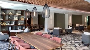A modern interior with a wooden ceiling, pendant lighting, a dining area with pink chairs, and a patterned rug.
