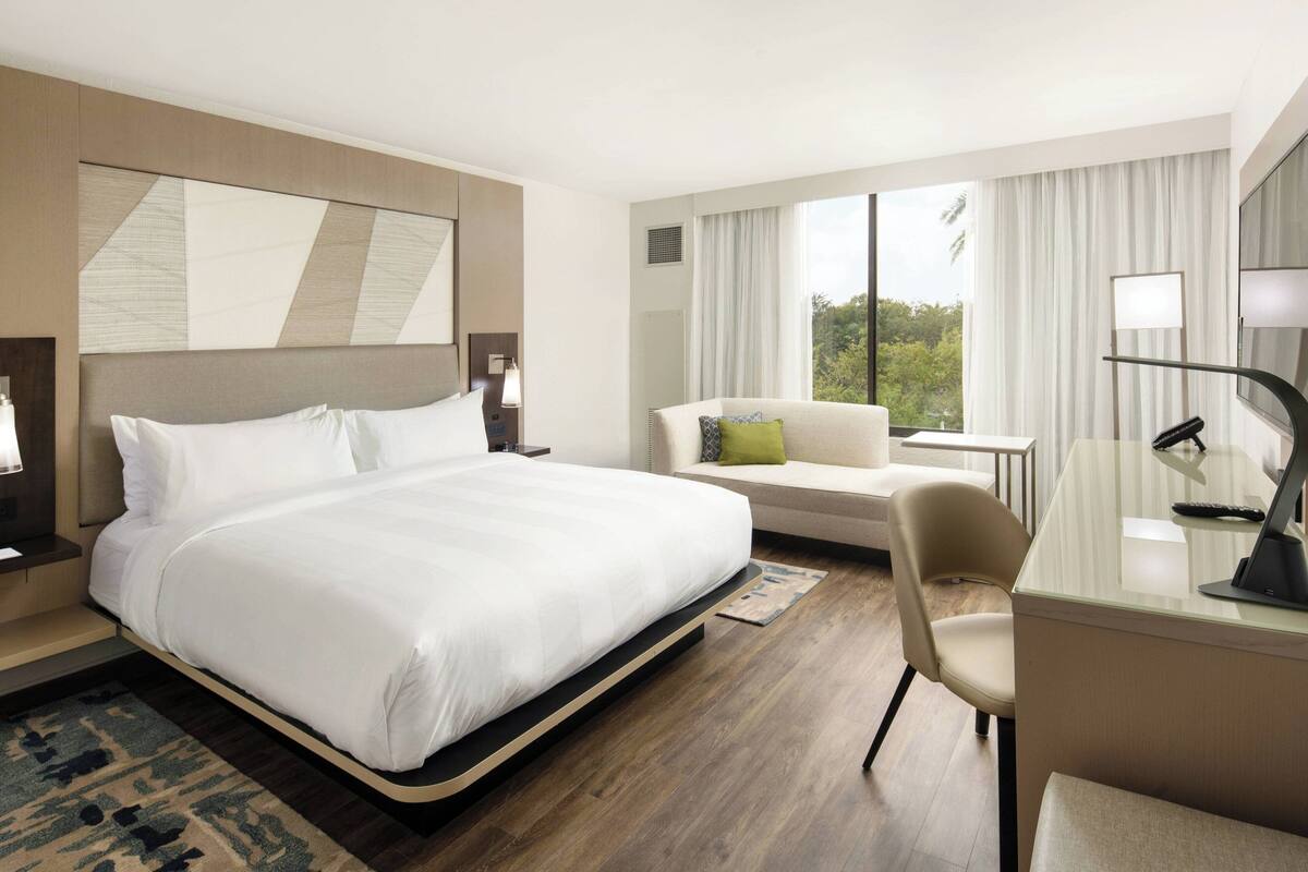 Een hotelkamer met een groot bed, een bureau, een stoel en uitzicht op de omgeving.