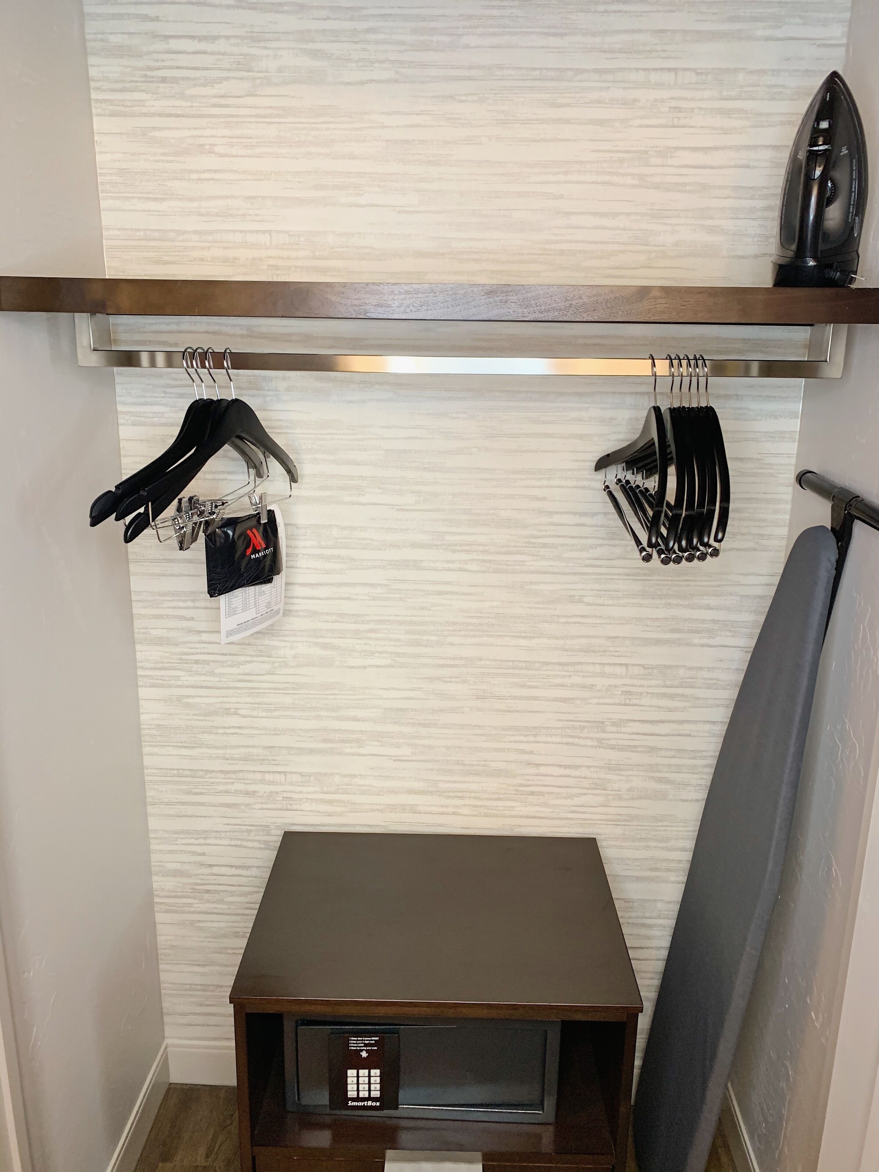A hotel room with a wooden shelf holding a black iron and a set of black utensils. Below the shelf, there's a SmartBox device on a small wooden table.