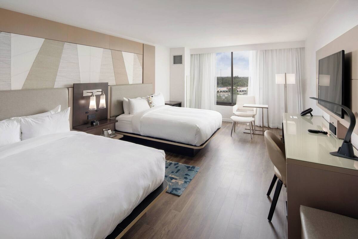 Een hotelkamer met twee bedden, een bureau met een televisie en uitzicht op de stad.