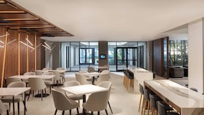 A modern dining area with multiple tables and chairs, large windows, and a view of the outdoors.