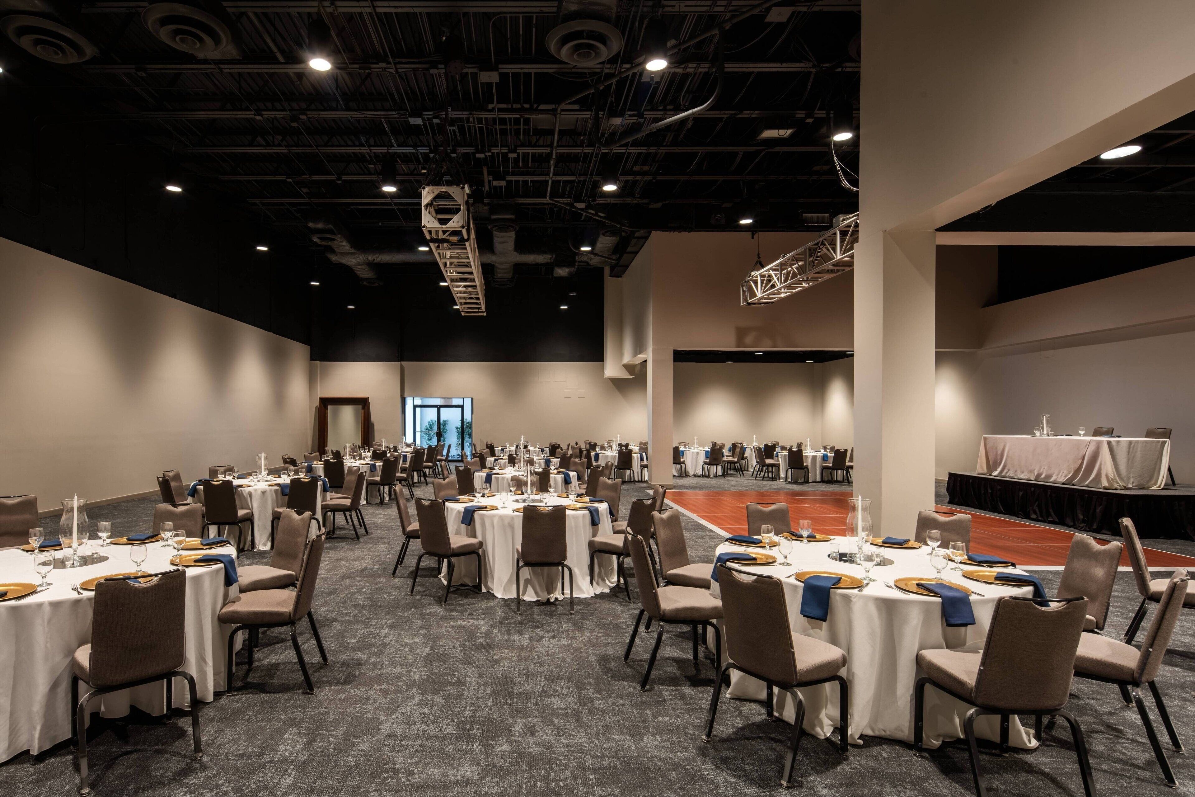 A large conference room with multiple round tables, each set with chairs and tableware.