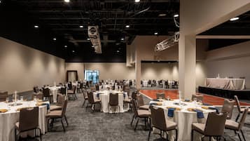 A large conference room with multiple round tables, each set with chairs and tableware.
