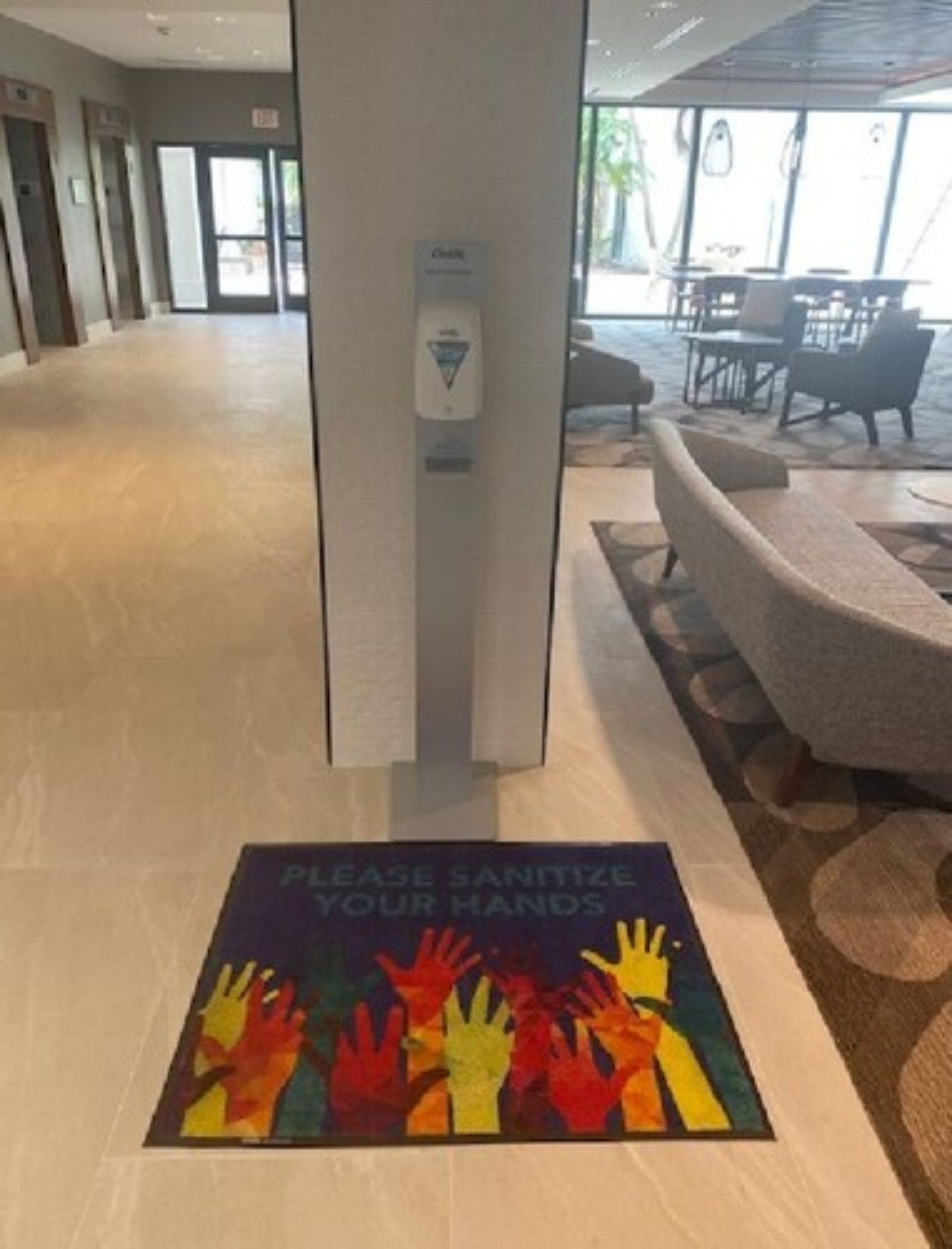 A hotel lobby with a hand sanitizer dispenser and a hand sanitizing sign on the floor.