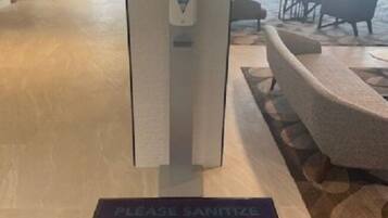 Een hotel lobby met een handdesinfecteerdispenser en een bord met instructies voor handdesinfectie op de vloer.