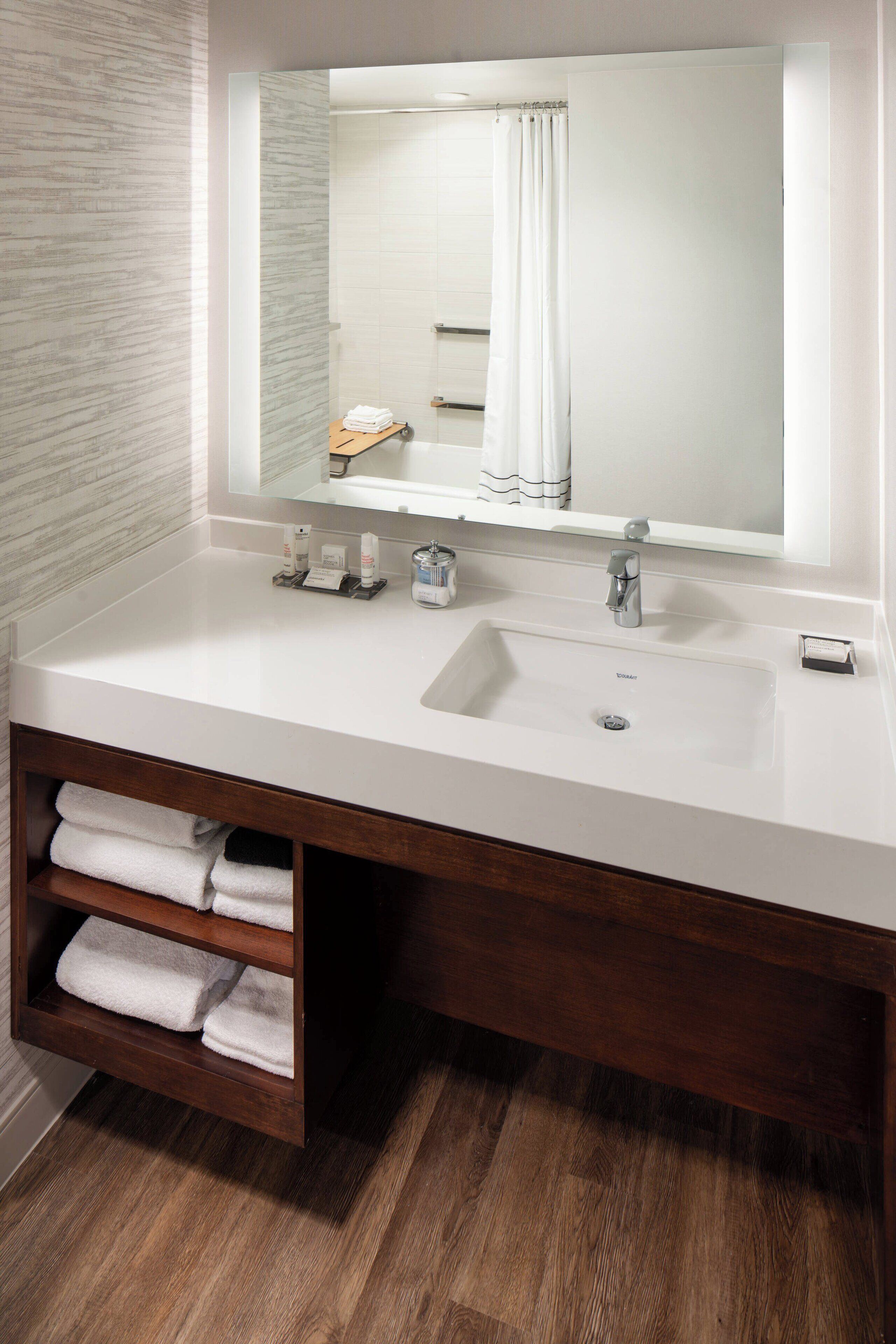 Un baño moderno con un lavamanos blanco, un espejo grande y un mueble de tocador de madera con estantes que sostienen toallas.