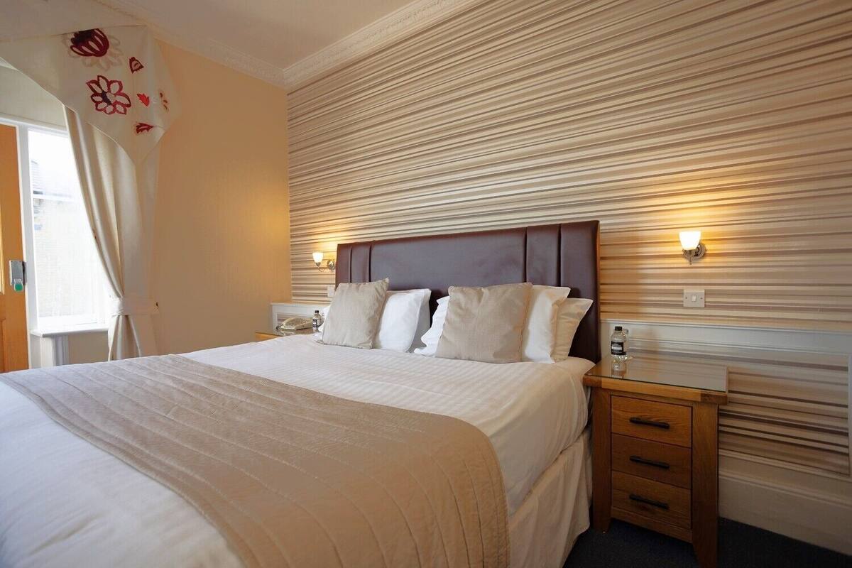 A hotel room with a large bed, a wooden headboard, two bedside tables with lamps, and a window with curtains.