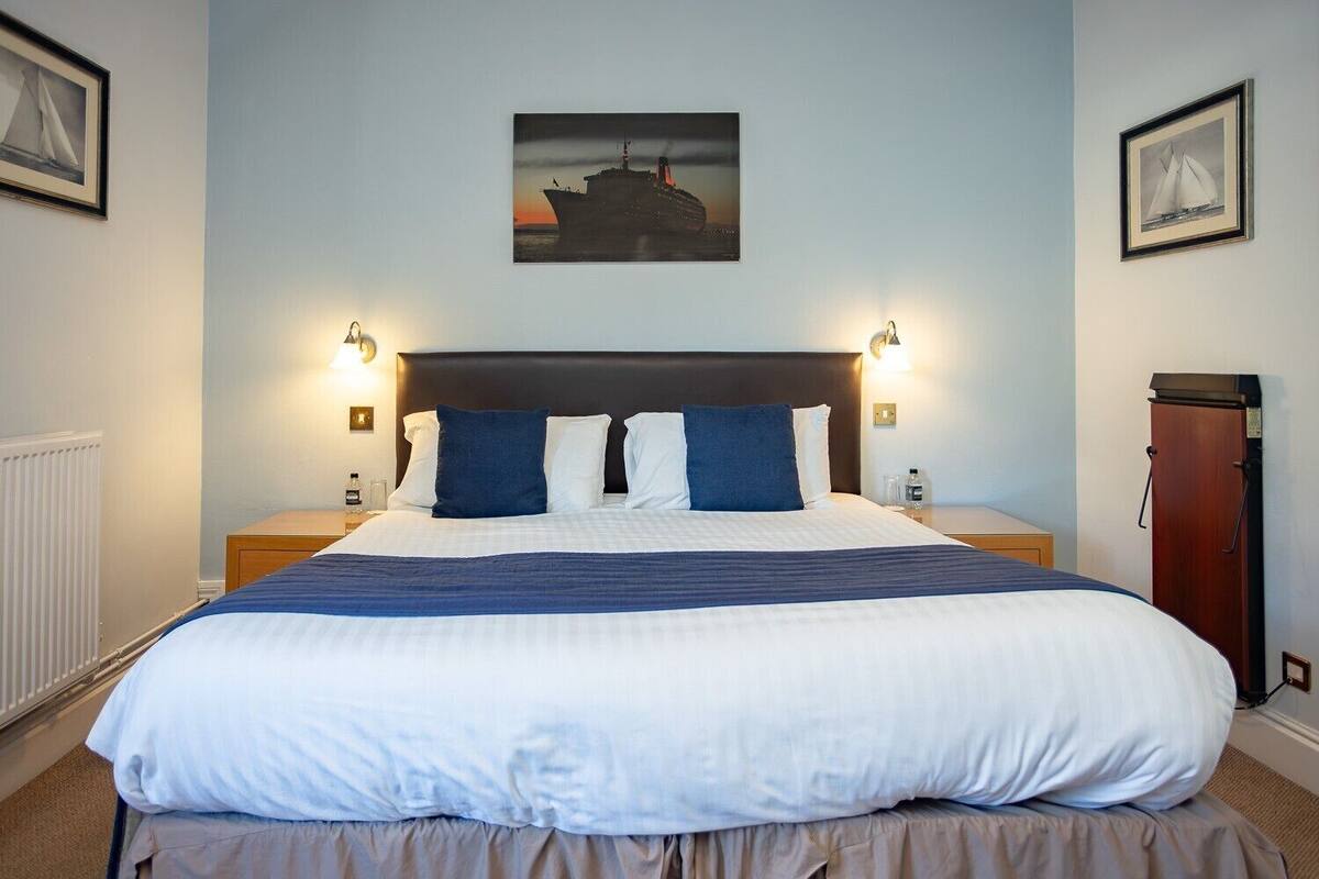 A hotel room with a large bed, two bedside tables, a headboard, and a framed picture of a ship on the wall.