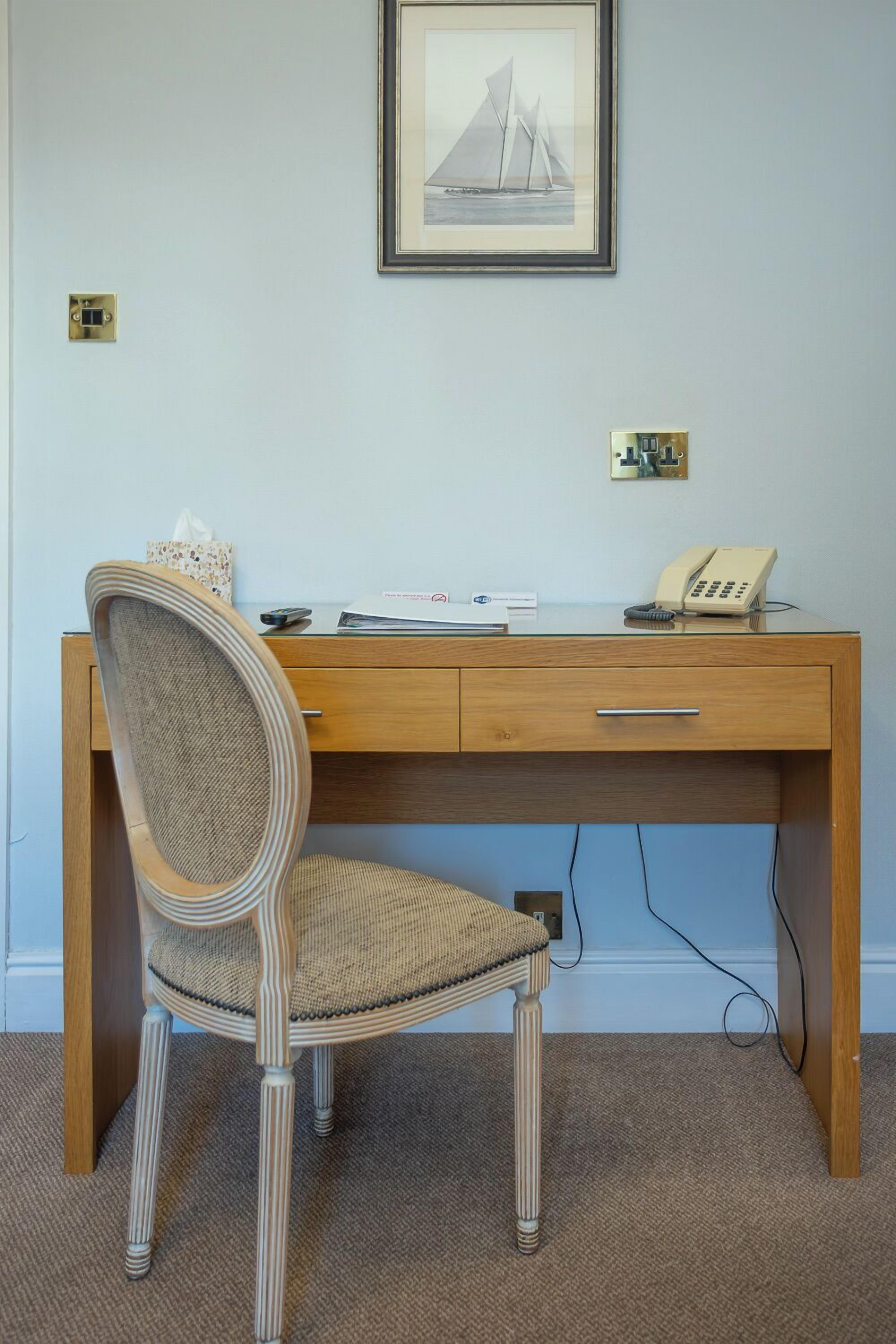A wooden desk with a chair, a framed picture on the wall, and a telephone.
