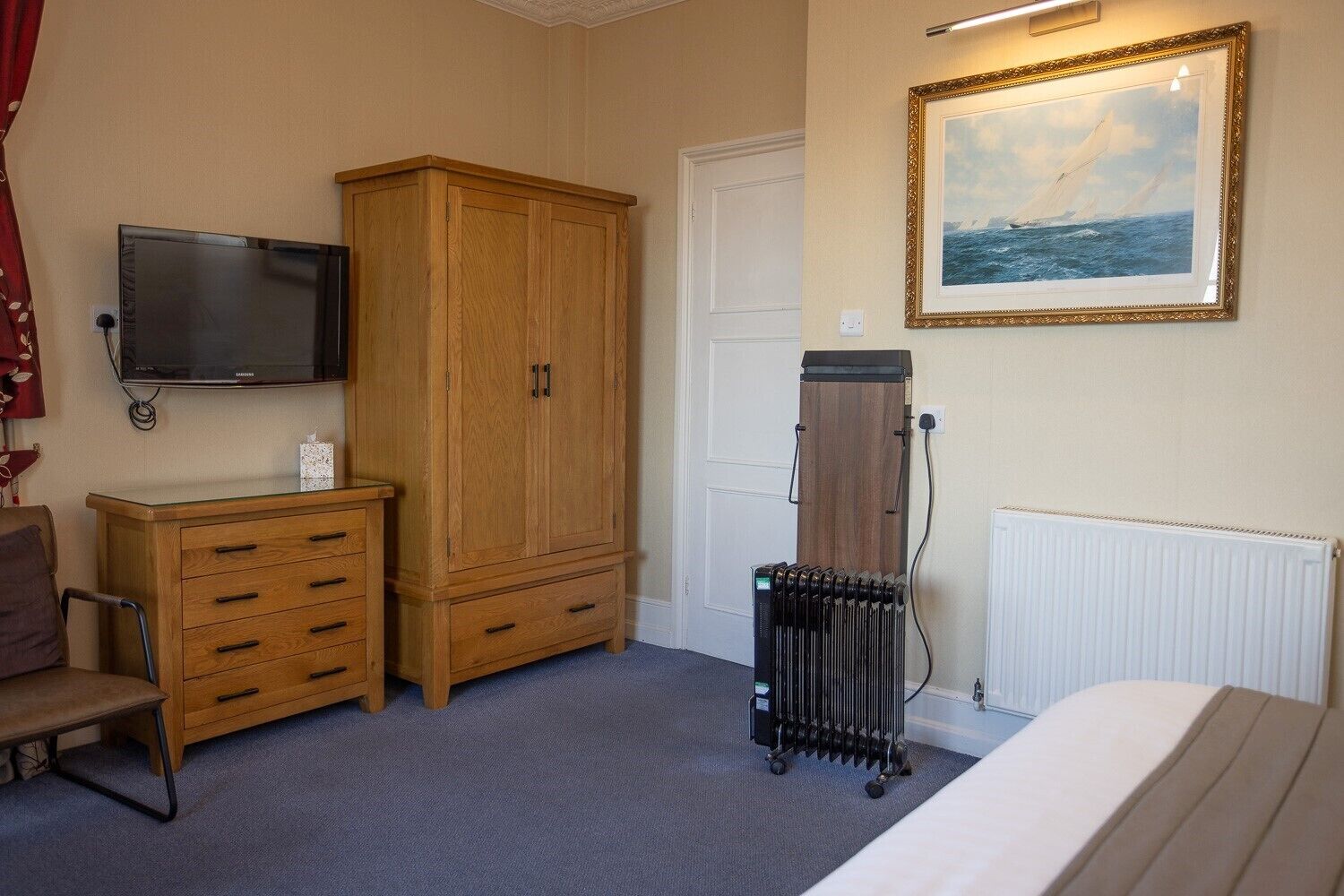 Ein Schlafzimmer mit Bett, Holzschrank, Fernseher, Heizkörper und einem gerahmten Bild an der Wand.