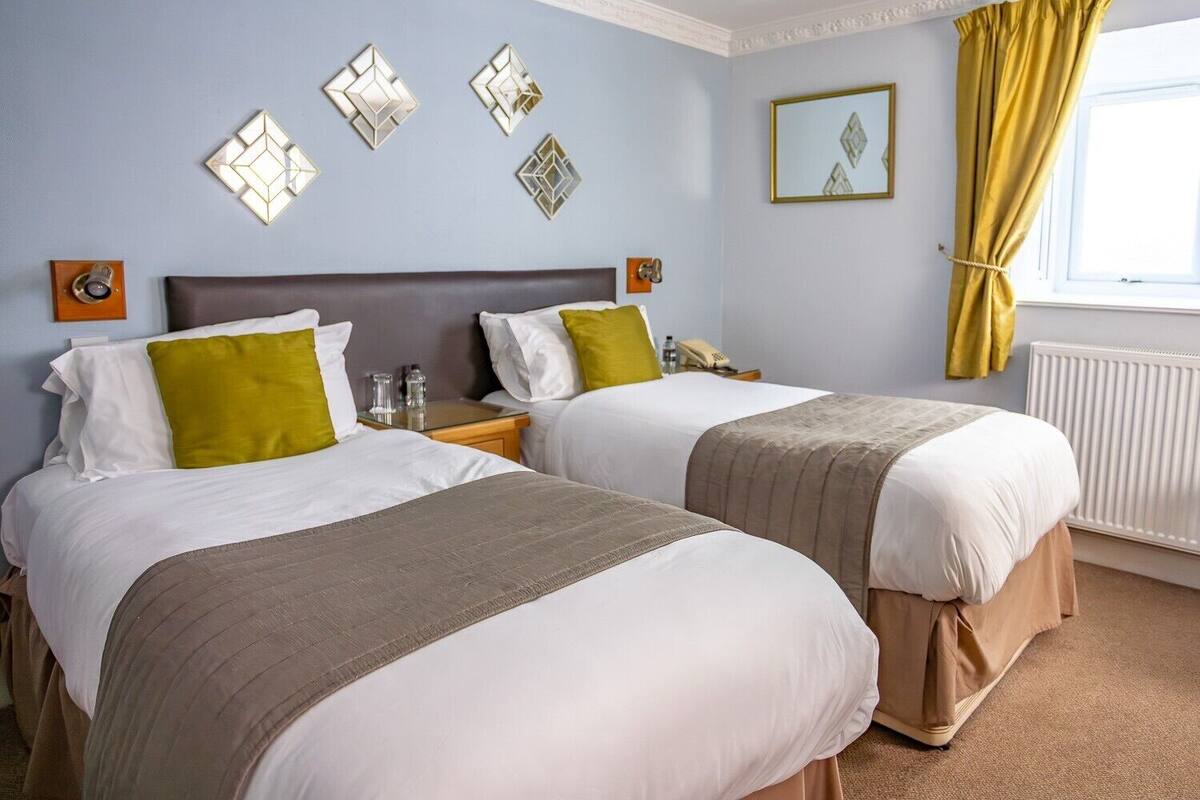 A hotel room with two beds, a nightstand, a mirror, and decorative wall art.
