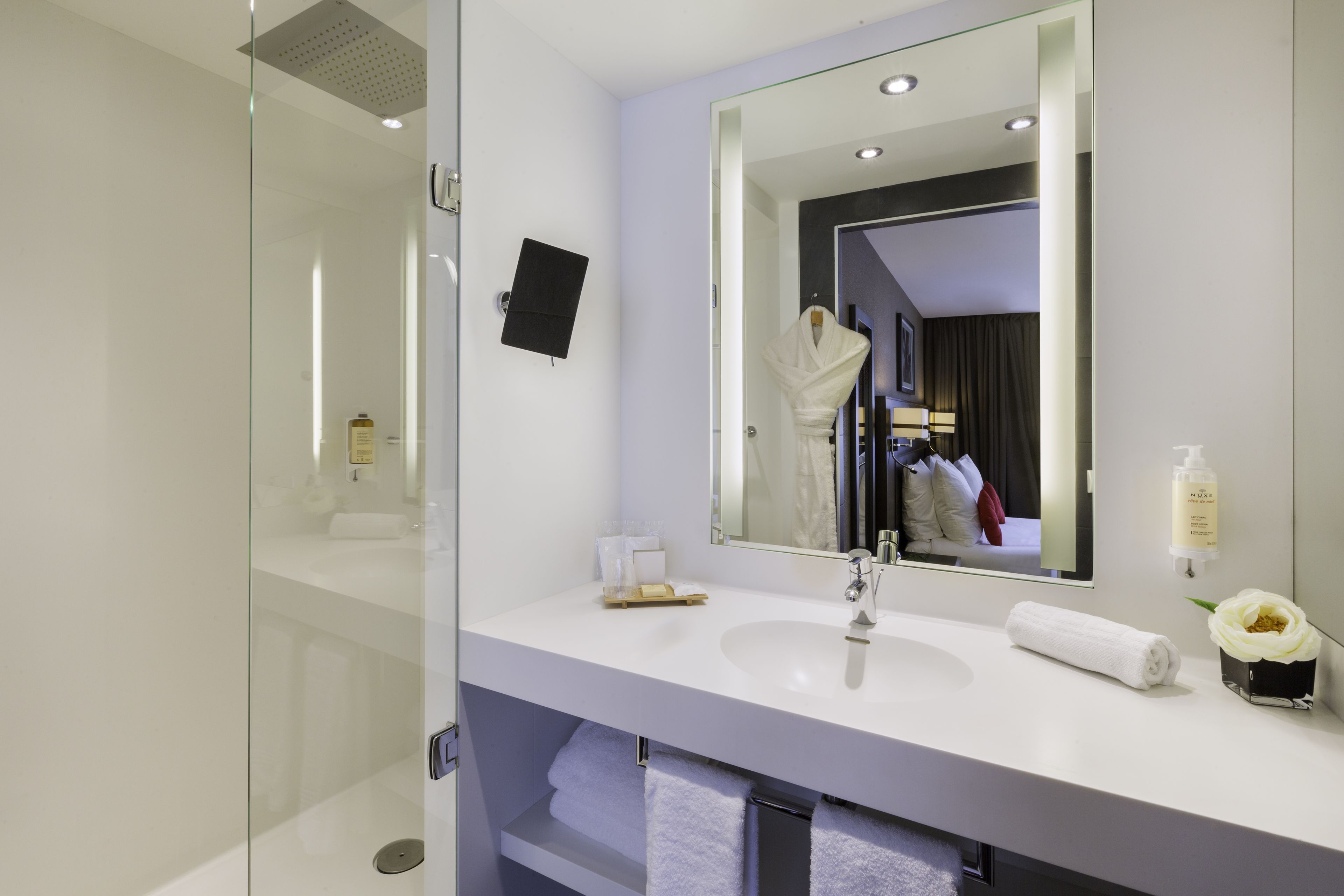 Ein modernes Badezimmer mit Duschkabine aus Glas, einem weißen Waschbecken und einem großen Spiegel.