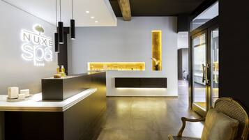 Un espace d’accueil moderne pour un spa, comprenant un comptoir de réception, un coin salon et une grande fenêtre.