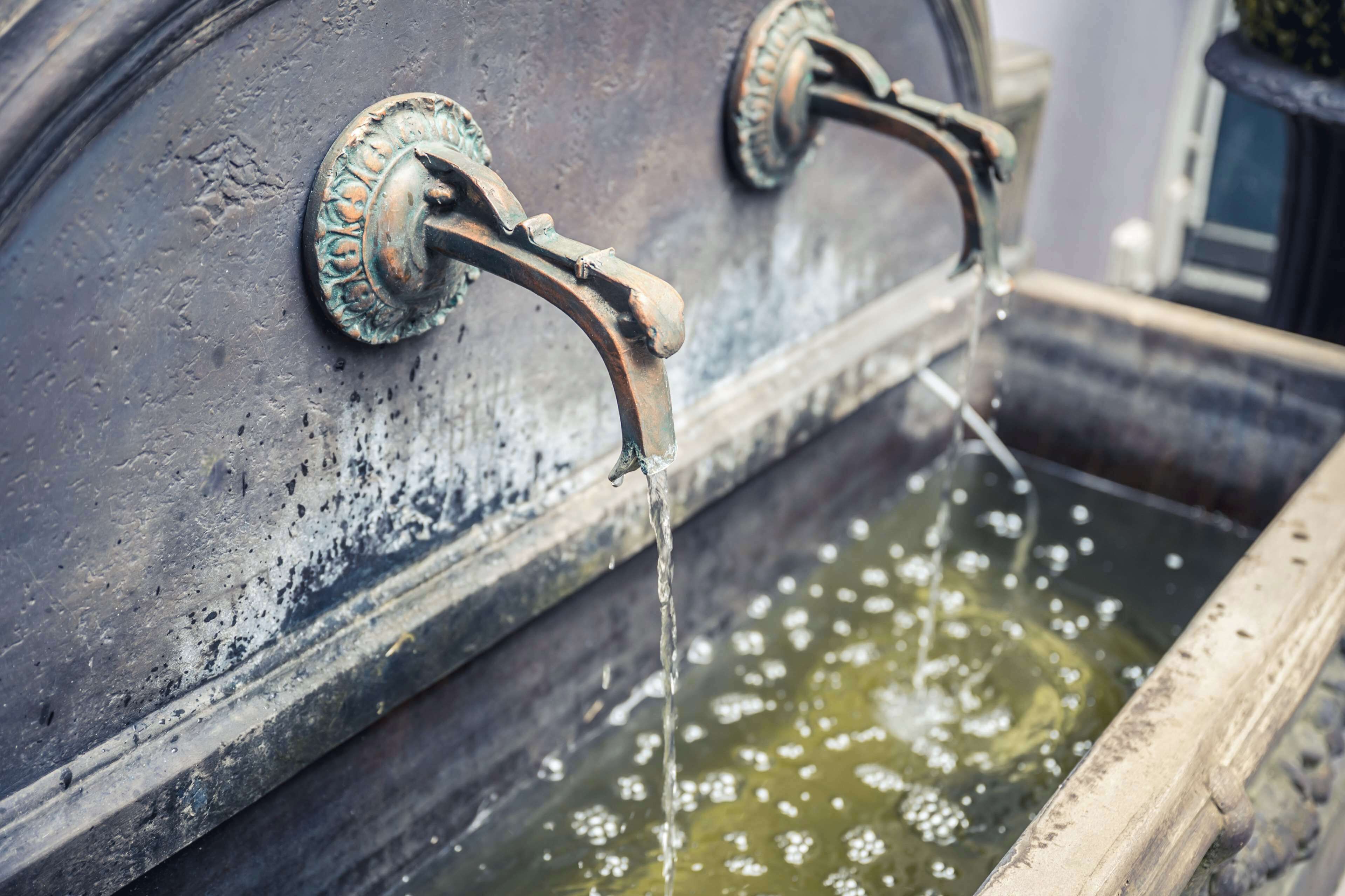 A water feature with two metal spouts and a basin.