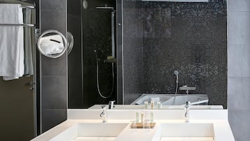Une salle de bain moderne avec un grand miroir, deux lavabos, une douche avec une porte en verre et un mur décoré de mosaïques.