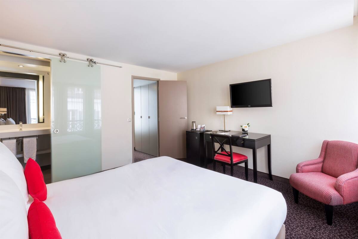 Hotellihuone, jossa on sänky, työpöytä, tuoli, televisio ja peili.